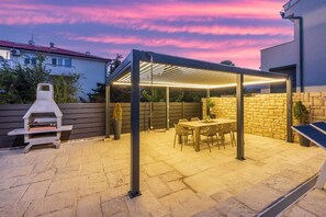 Une terrasse extérieure équipée d’un barbecue, d’une table et de chaises, le tout entouré d’un mur en pierre et d’une clôture en bois.