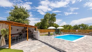 A backyard with a brick barbecue, outdoor seating, a swimming pool, and a wooden fence. - Holiday house Meri with a heated Pool (Gabonjin (Krk))