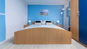 A bedroom with a wooden bed, two bedside tables with lamps, a blue wall, and a painting. - Holiday house Meri with a heated Pool (Gabonjin (Krk))