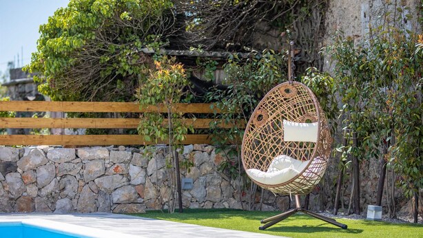 A wicker egg chair by a pool with a stone wall and wooden fence in the background. - Holiday house Meri with a heated Pool (Gabonjin (Krk))