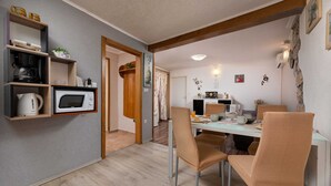 A compact kitchen with a microwave, kettle, and coffee maker on shelves, a dining table with chairs, and a small refrigerator. - Holiday house Meri with a heated Pool (Gabonjin (Krk))