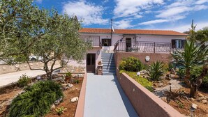 A two-story house with a red-tiled roof, a stone pathway leading to the entrance, and a small garden with various plants and a palm tree. - Holiday house Meri with a heated Pool (Gabonjin (Krk))