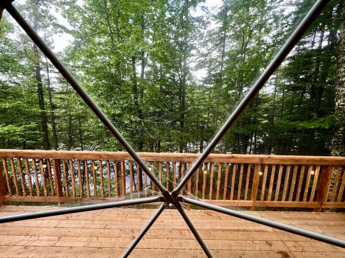Une terrasse en bois avec une rambarde en métal, entourée d’une zone boisée.