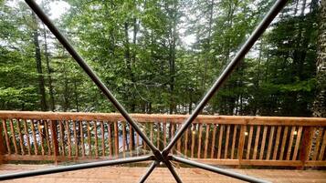 Une terrasse en bois avec une rambarde en métal, entourée d’une zone boisée.