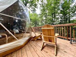 Une terrasse en bois surmontée d’une structure transparente en forme de tente, avec une chaise en bois et une balustrade en bois.