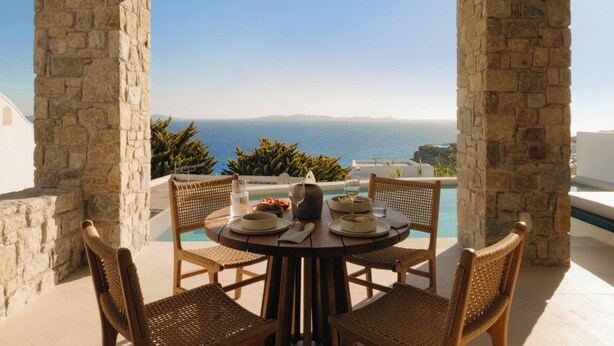 A table set for two with a view of the sea, stone pillars, and a pool. - Bard De Sol (Mykonos)