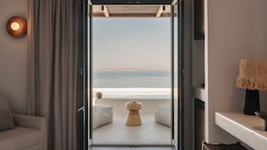 An open door leading to a balcony with a view of the sea, a sofa, and a small table with a vase. - Bard De Sol (Mykonos)