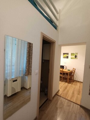 A room with a wooden floor, a mirror, a door leading to another room, and a dining area with a table and chairs.