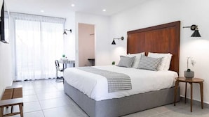 A modern bedroom with a large bed, a small table, and a chair. There is a window with curtains and a lamp on the wall. - HOTEL VISTA LAGO (La Pena)