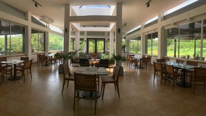 A spacious dining area with high ceilings, large windows, and natural light. Tables are set with chairs and centerpieces. - HOTEL VISTA LAGO (La Pena)