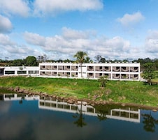 Un hotel de varios pisos con balcones, piscina y reflejo en el agua.