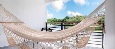 A hammock suspended between two white walls in a room with a balcony.