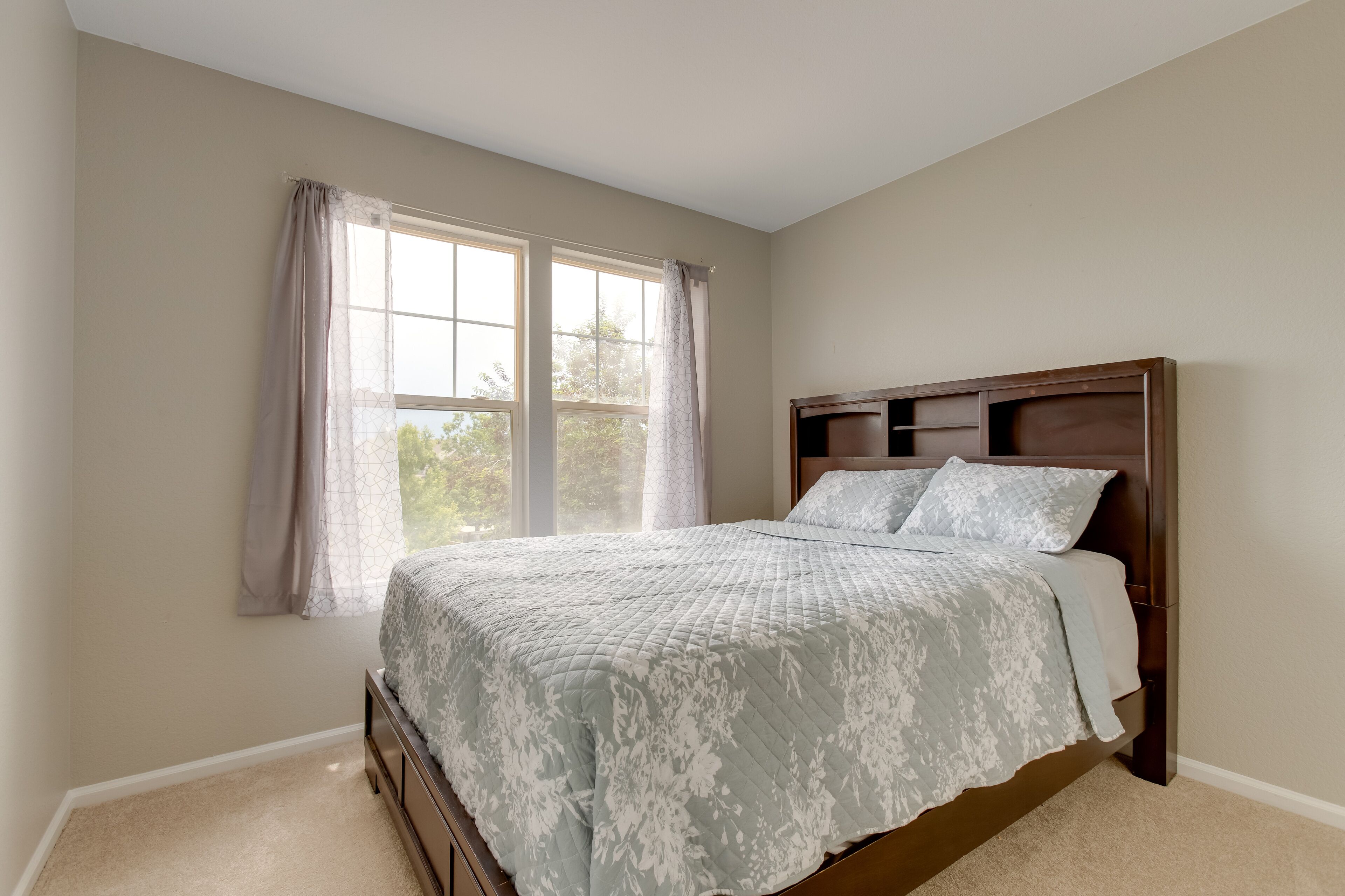 A bedroom with a bed, a window with curtains, and a headboard.