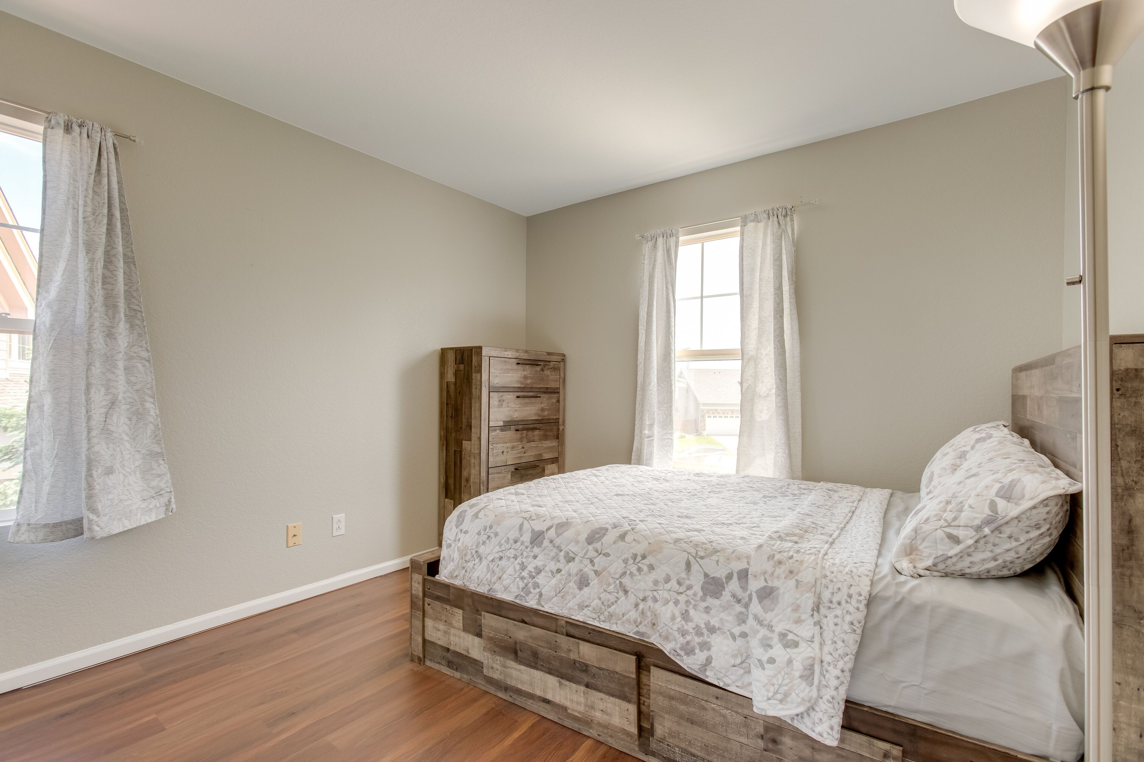 A bedroom with a wooden bed frame, a nightstand, and a window with curtains.