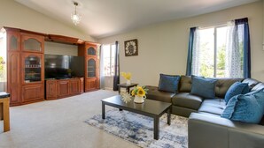 Ein Wohnzimmer mit Sofa, Couchtisch, Fernseher, Holzkredenz und einer Kronleuchter.