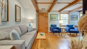 Una sala de estar con sofá, dos sillones, una mesa de centro, piso de madera y una puerta de madera.