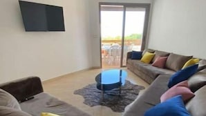 Un salon moderne avec un grand canapé, une table basse et un téléviseur à écran plat fixé au mur.