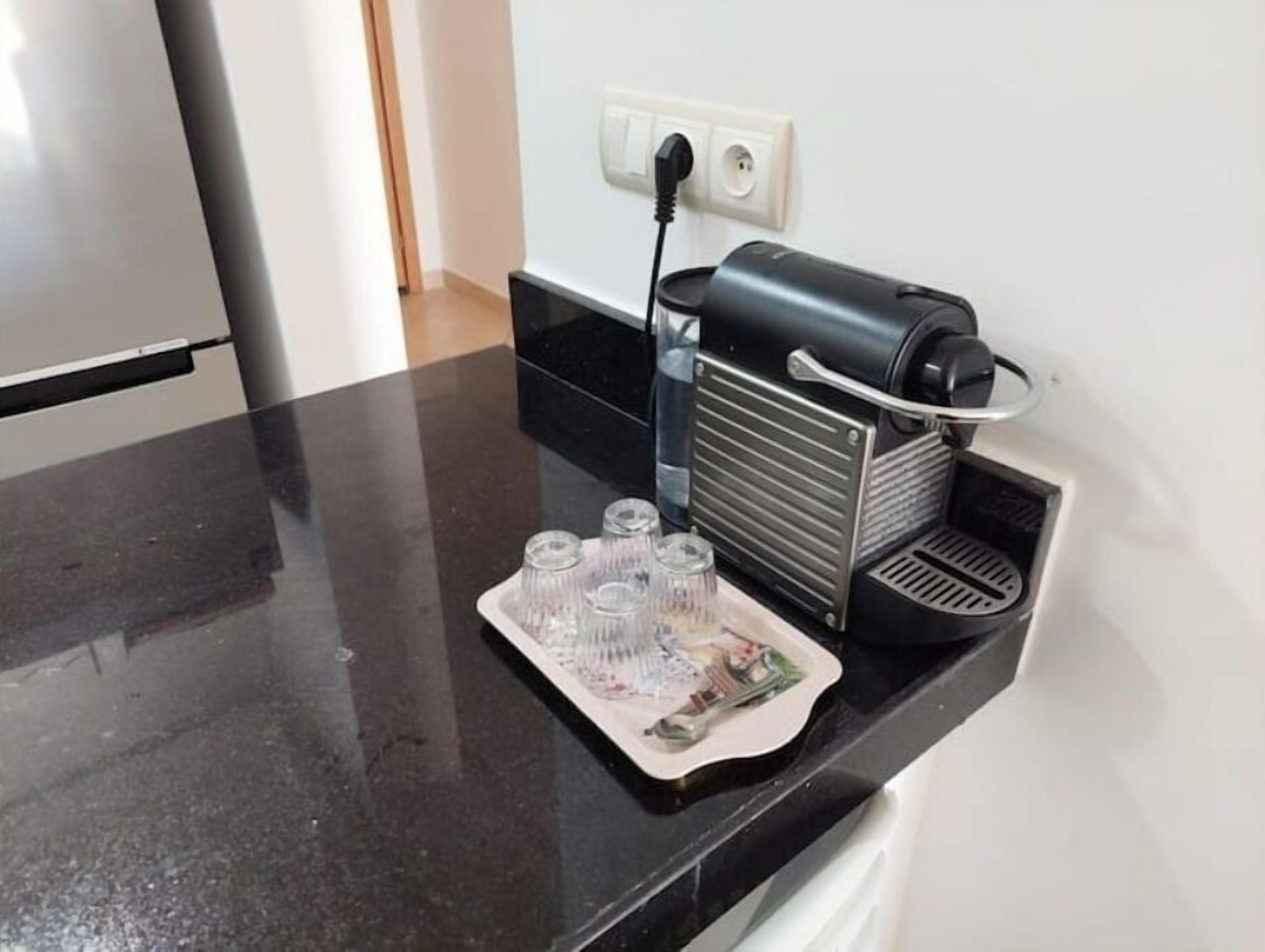 A kitchen counter with a coffee maker, a power outlet, and a tray with cups and a spoon.