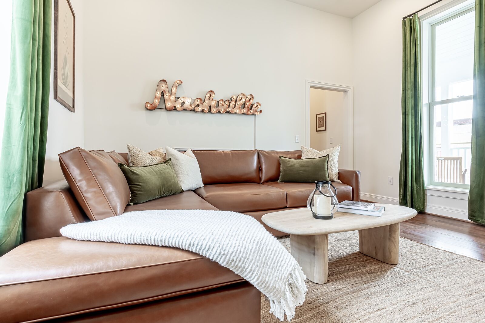 Ett modernt vardagsrum med en brun lädersoffa i sektionsmodell, ett soffbord och en väggmonterad skylt med texten ”Nashville”.