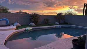 Un jardin avec une piscine, un mur en pierre et un palmier.