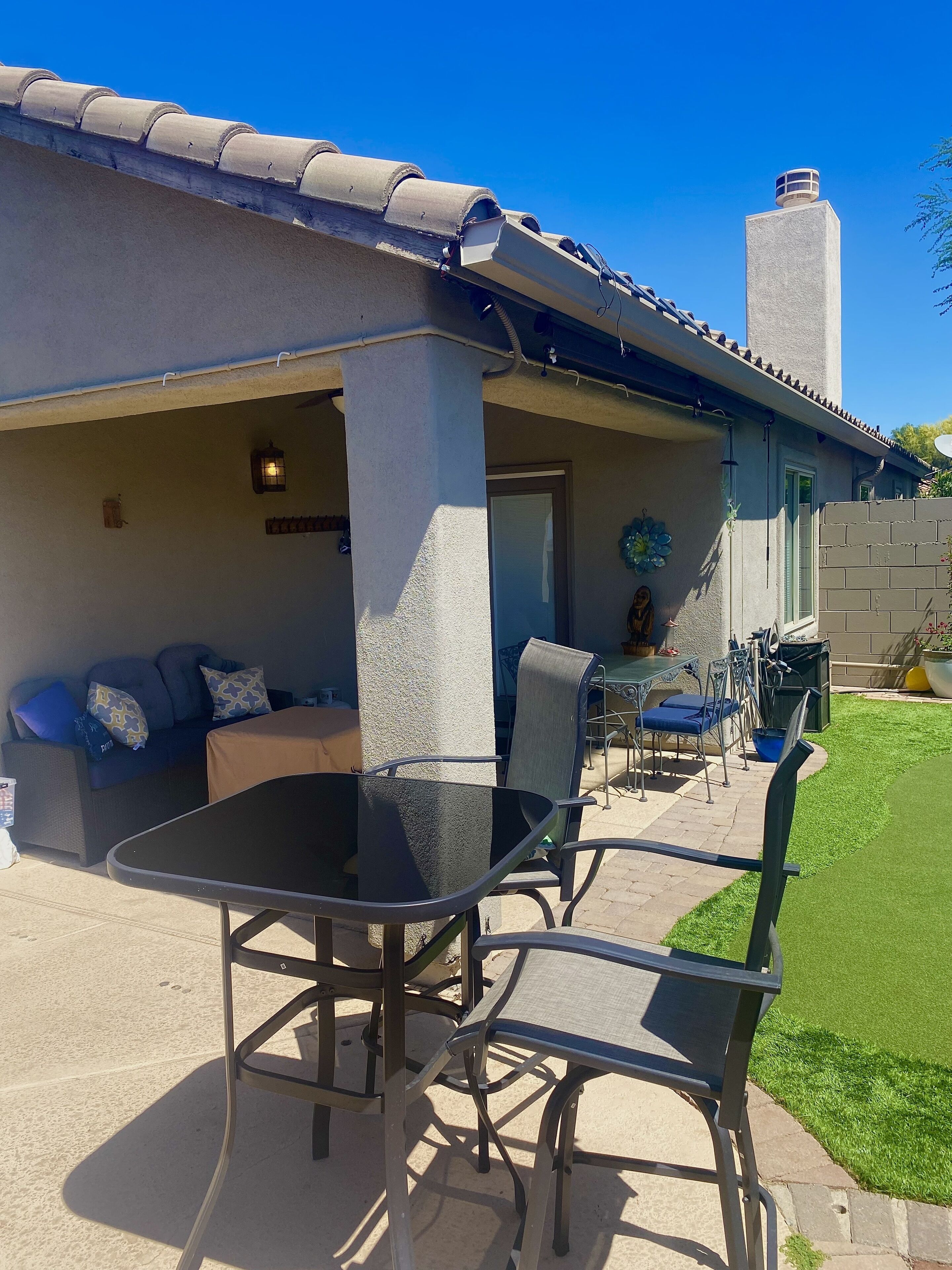 An outdoor patio with a table and chairs, a covered seating area, and a view of a building with a chimney.