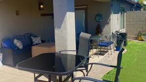 Une terrasse extérieure avec une table et des chaises, un espace salon couvert et une vue sur un bâtiment doté d’une cheminée.