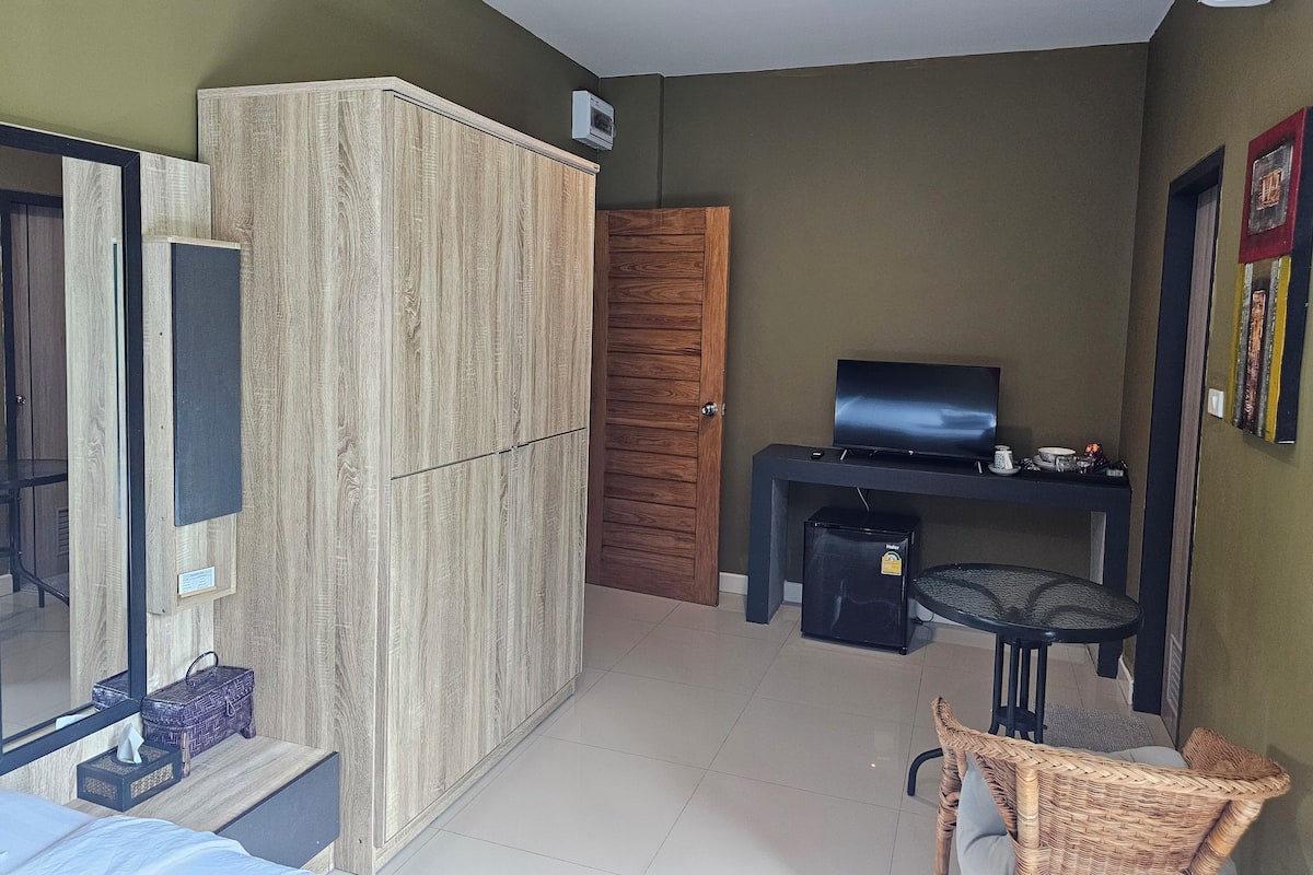 A compact room with a wardrobe, a television, a small table, and a wicker chair.