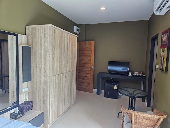 Une chambre de taille modeste, comprenant une armoire, un téléviseur, une petite table et une chaise en osier.