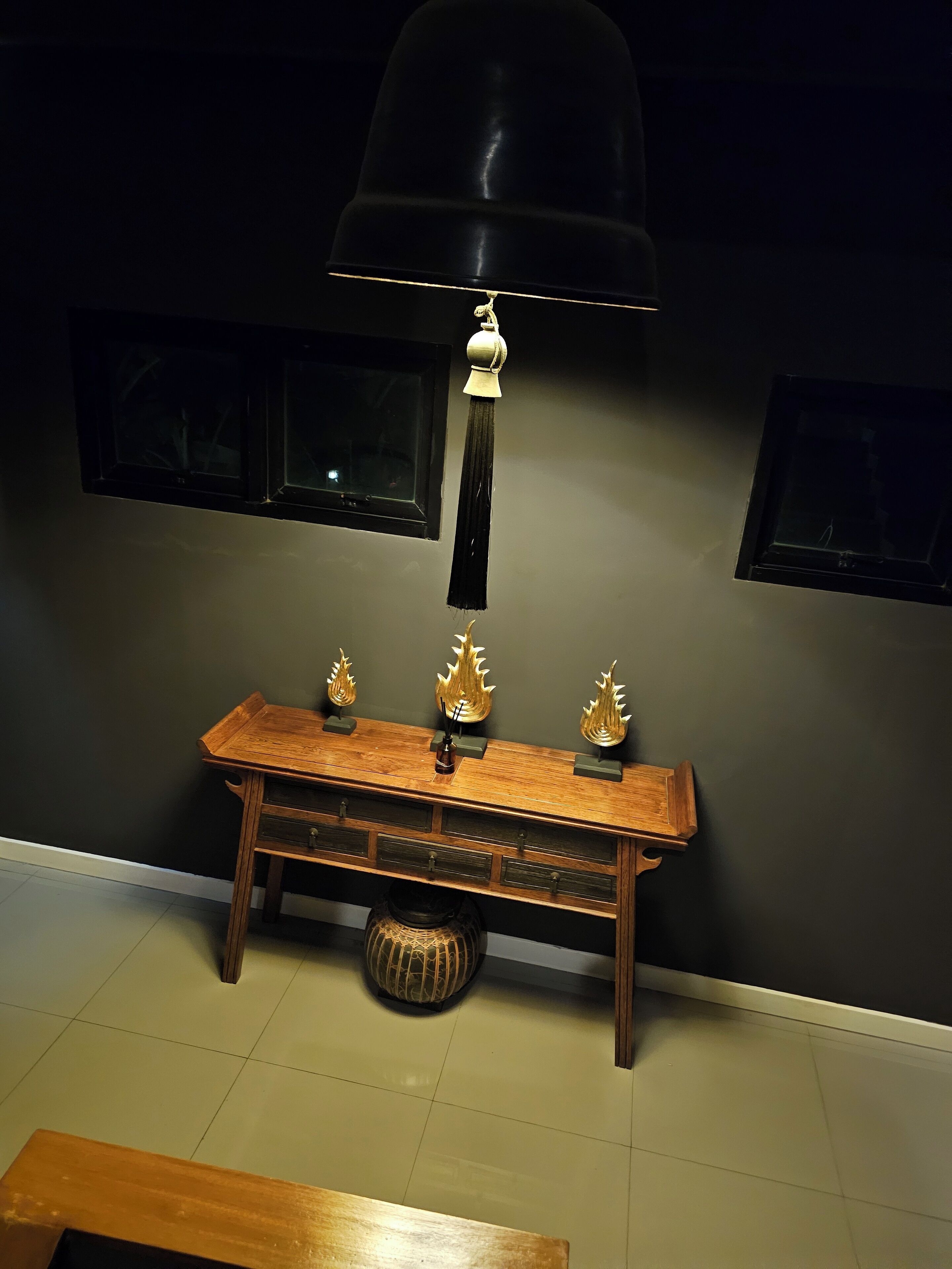 A wooden console table with three decorative items, a black pendant lamp, and a small round woven basket.