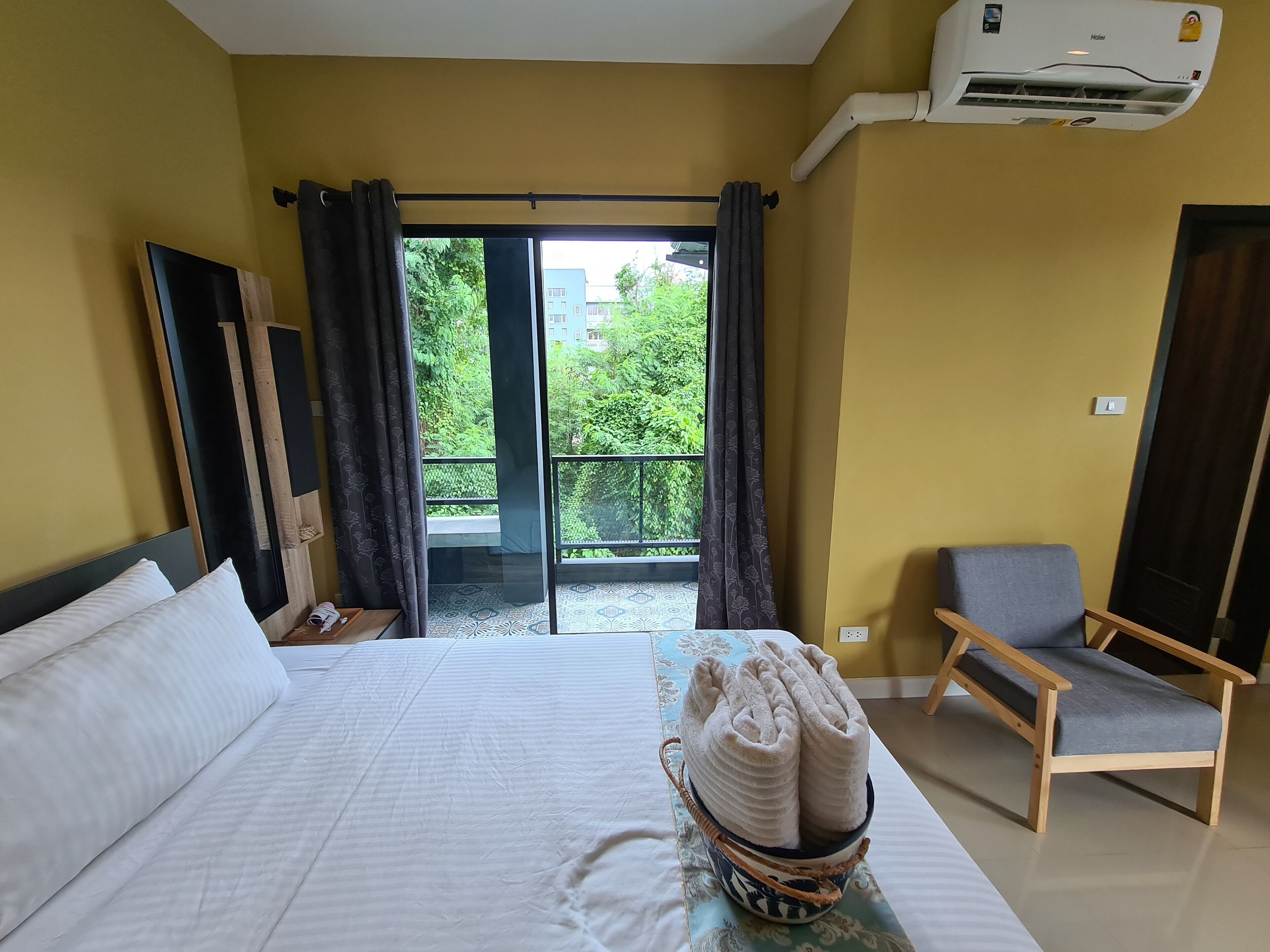 Une chambre d’hôtel avec un lit, une chaise, une fenêtre avec des rideaux et un balcon donnant sur un paysage verdoyant.