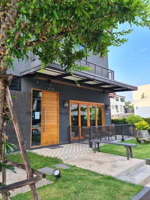 A modern building with a large wooden door, a balcony with outdoor furniture, and a well-maintained garden. - The Lantern Suites (Bangkok)