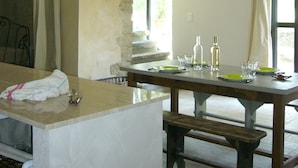 Une cuisine avec un mur en pierre, une table en bois dressée pour le repas et un lustre.