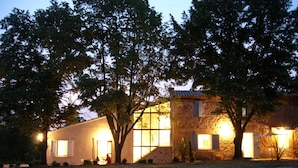 Une maison à deux étages avec une façade en pierre, de grandes fenêtres et un éclairage extérieur soigné au crépuscule.
