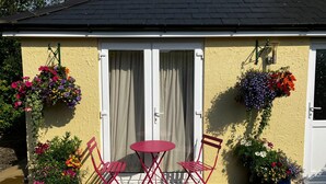 Un patio con una mesa y sillas rojas, una pared amarilla y cestas de flores colgantes.