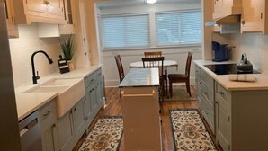 A narrow kitchen with a dining table and chairs, wooden cabinets, a window with blinds, and a hanging light fixture. - Spacious charming farmhouse-style home - dedicated office (Burlington)