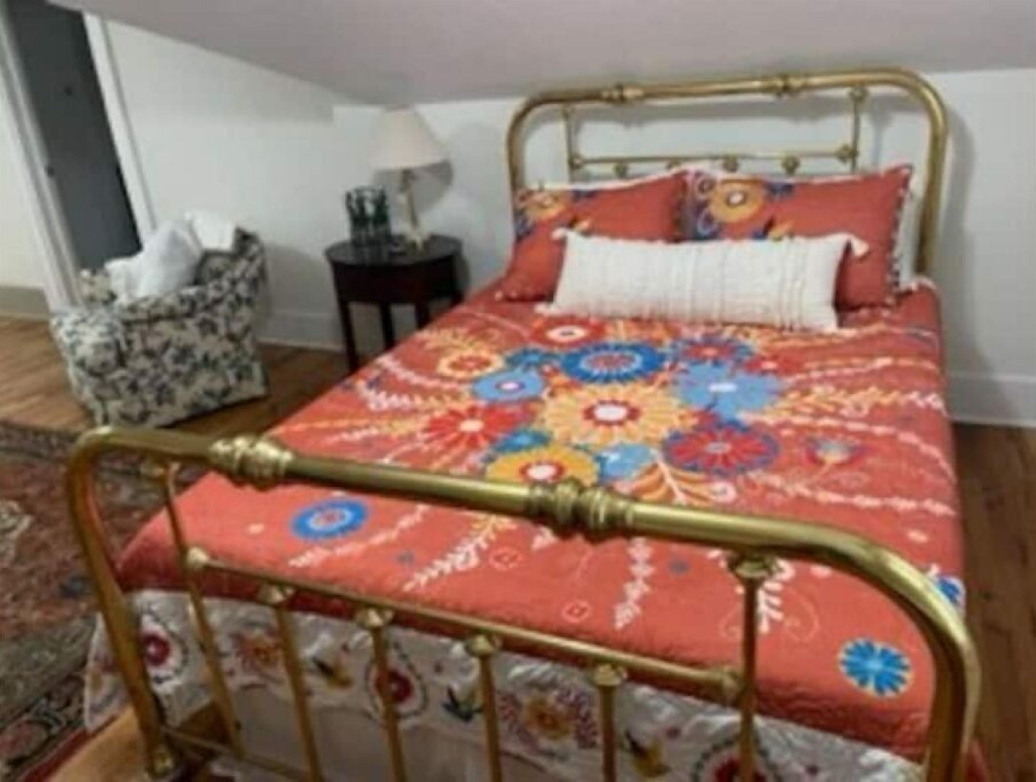 Una cama con una colcha estampada, un cabecero de metal y una mesita de noche con una lámpara.