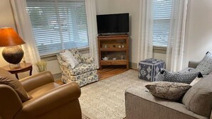 A living room with a brown leather sofa, a grey sofa, a patterned armchair, a wooden TV stand, and a small blue ottoman. - Spacious charming farmhouse-style home - dedicated office (Burlington)