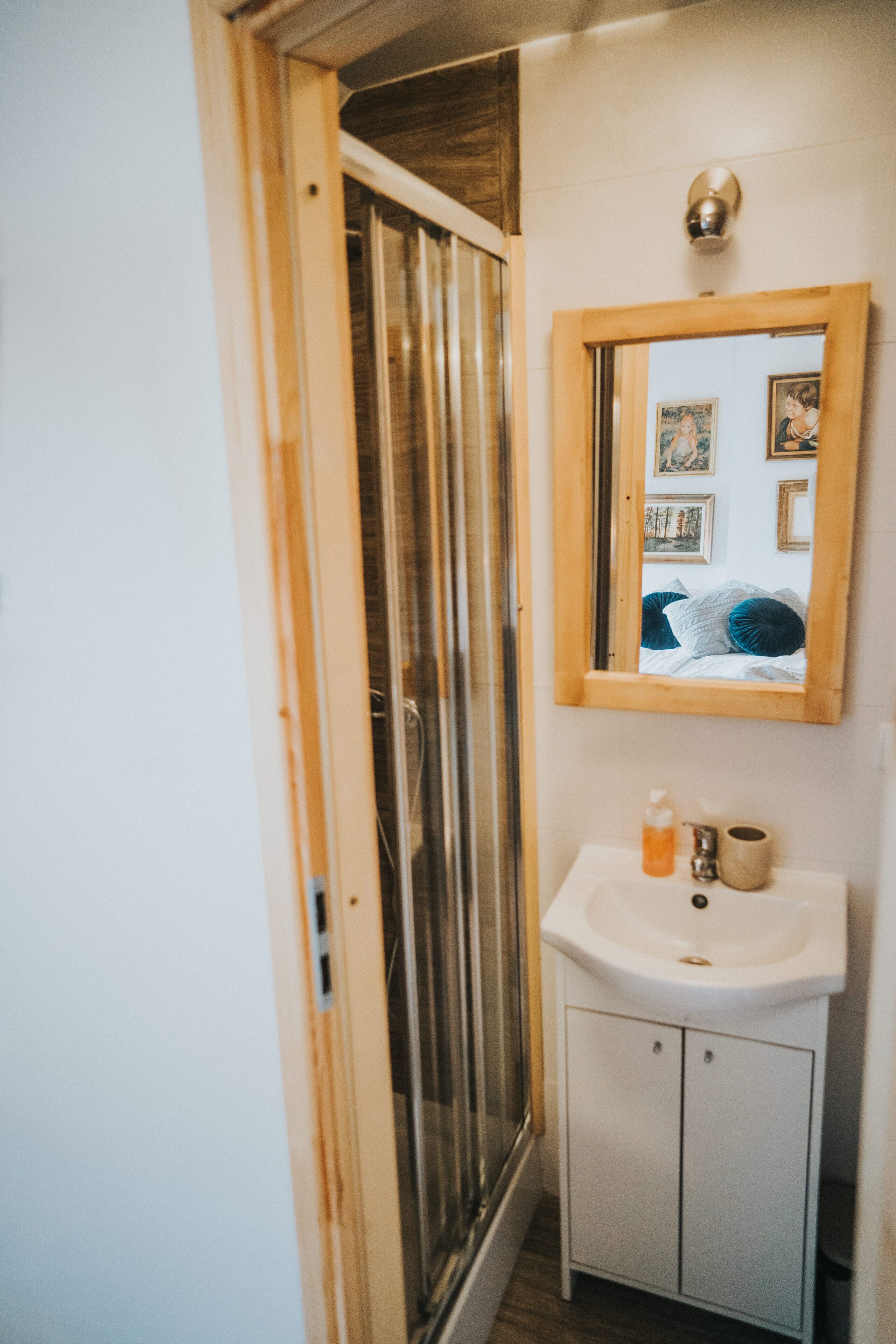 Een badkamer met een spiegel met houten lijst, een witte wasbak en een douchecabine.