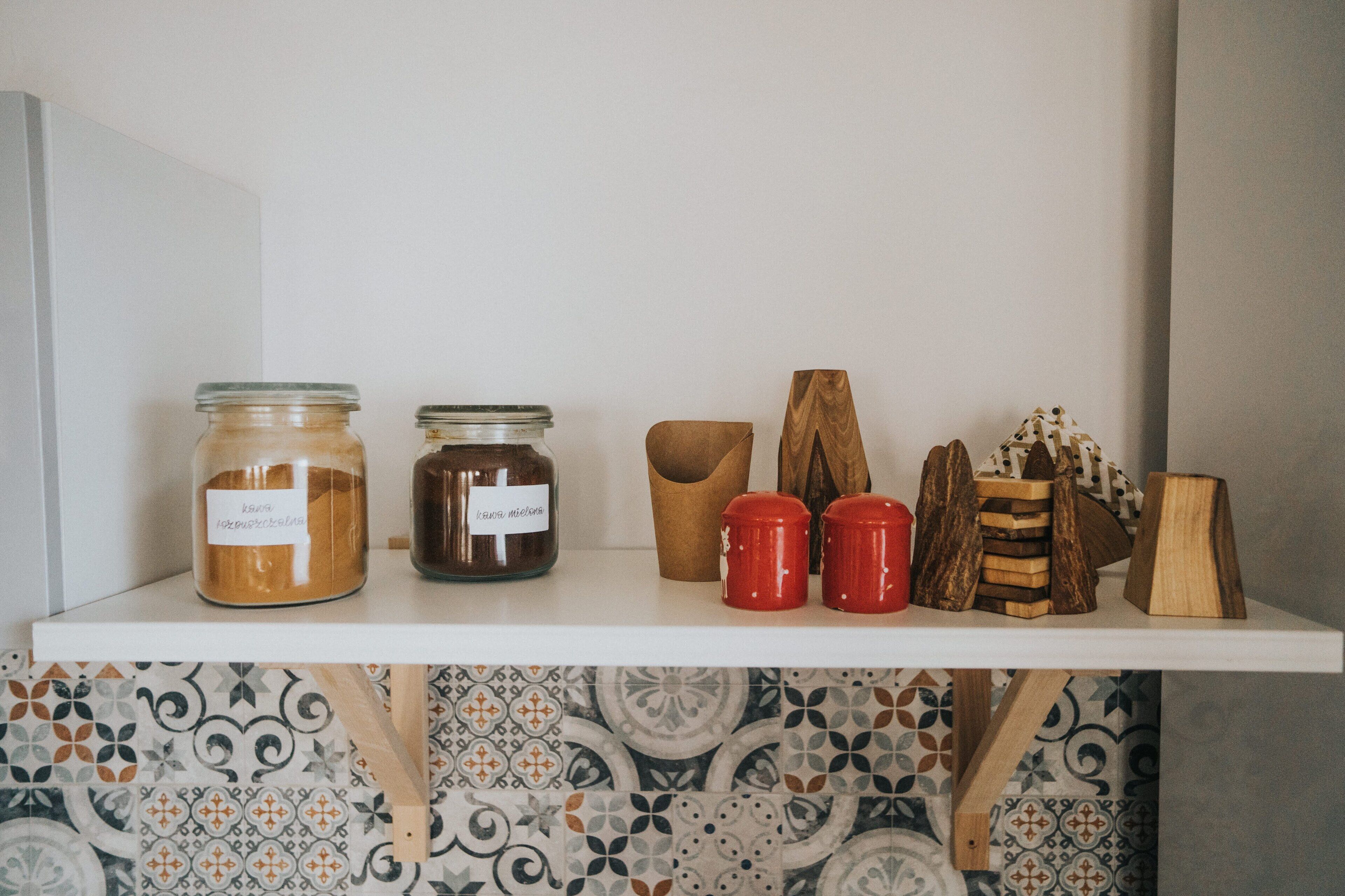A shelf with jars, a wooden bowl, and red containers.