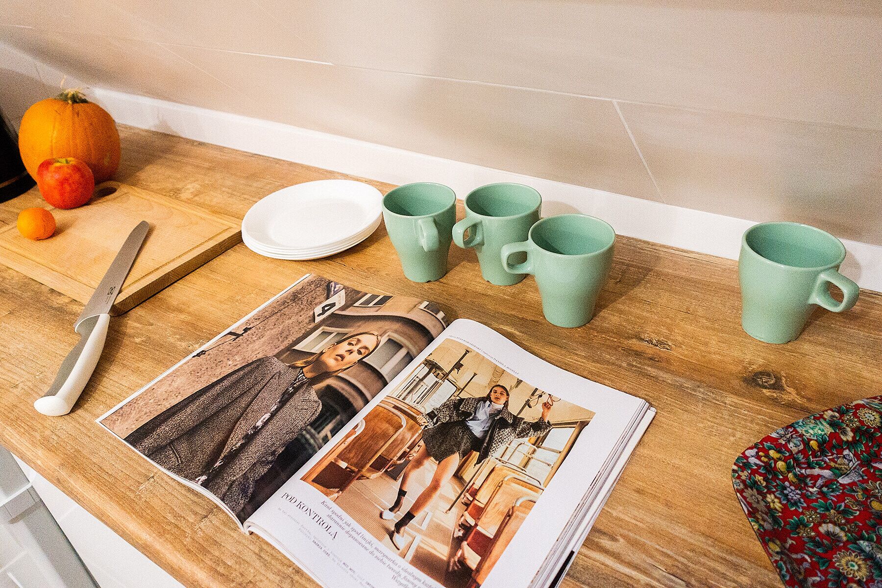 A kitchen counter with a knife, a plate, a magazine, and four green mugs.