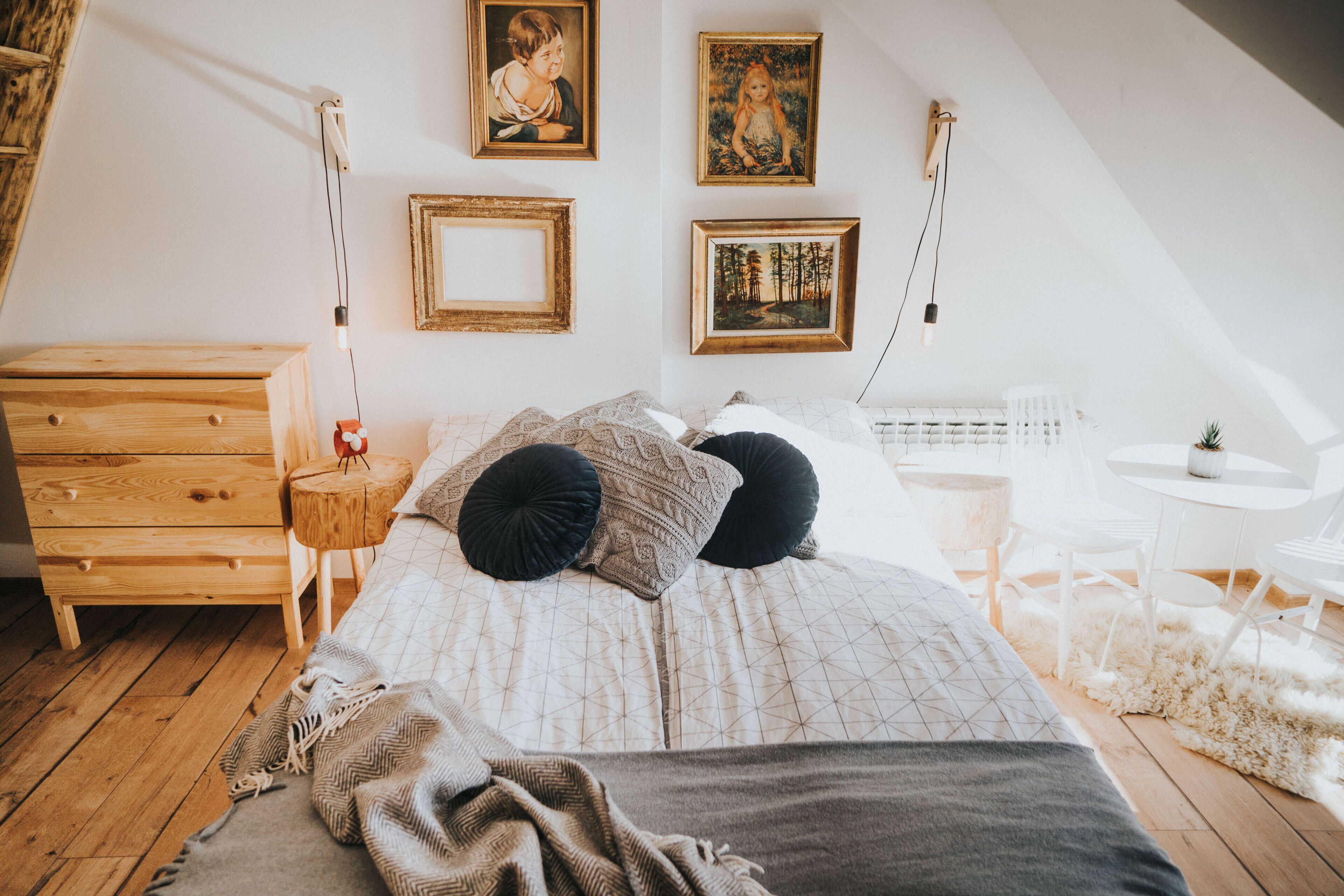 A bedroom with a wooden dresser, a bed with patterned bedding, and a small round table with a lamp.