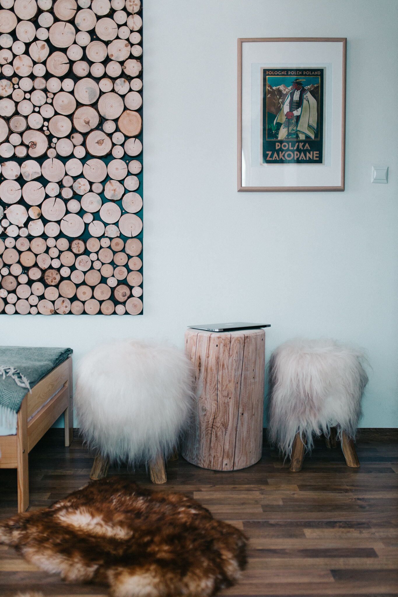 Una habitación con una obra de arte de leña montada en la pared, un cartel enmarcado, una cama de madera, dos taburetes mullidos y una alfombra de piel.