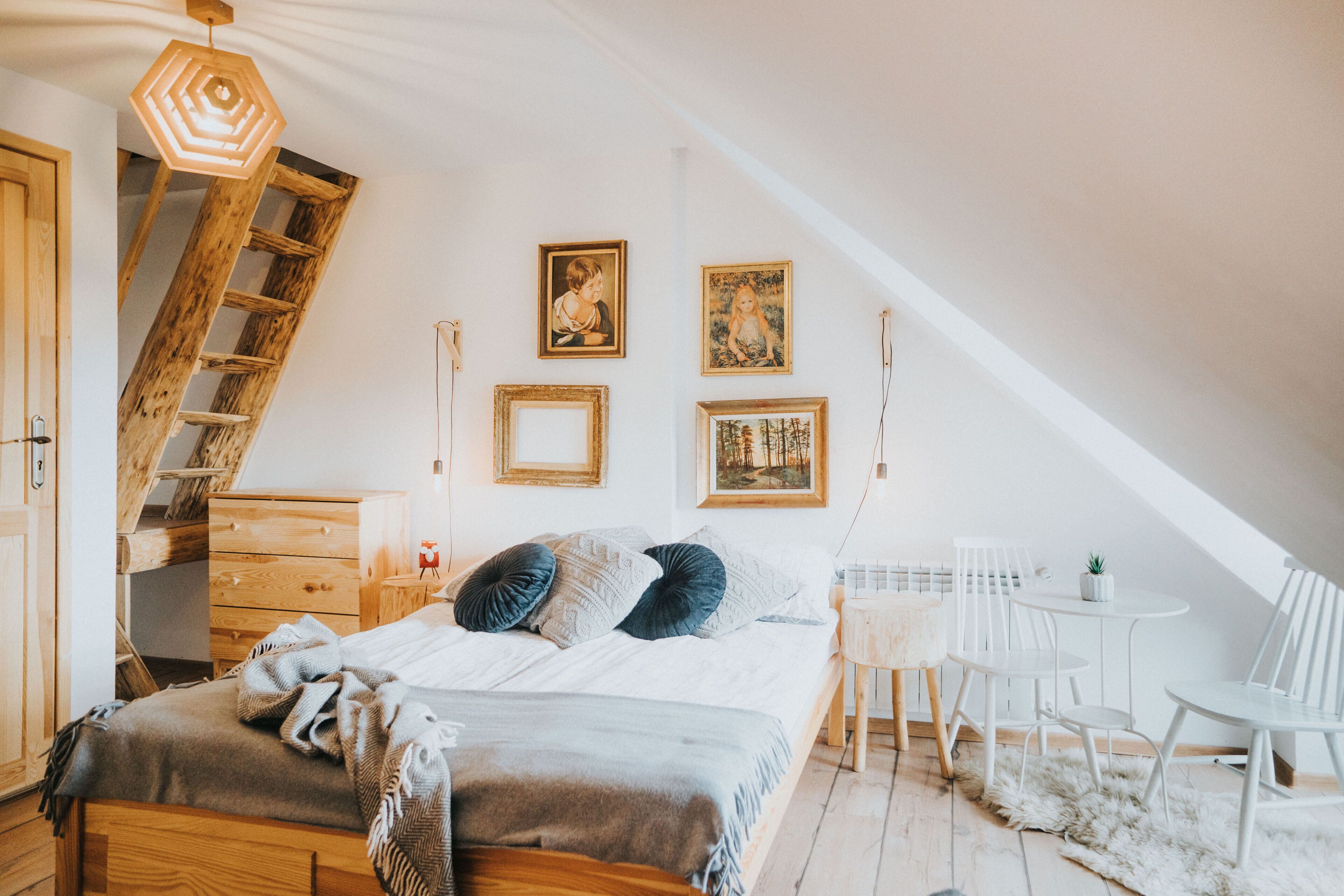 Une chambre avec un lit en mezzanine, une échelle en bois, une petite table avec des chaises et des tableaux encadrés au mur.