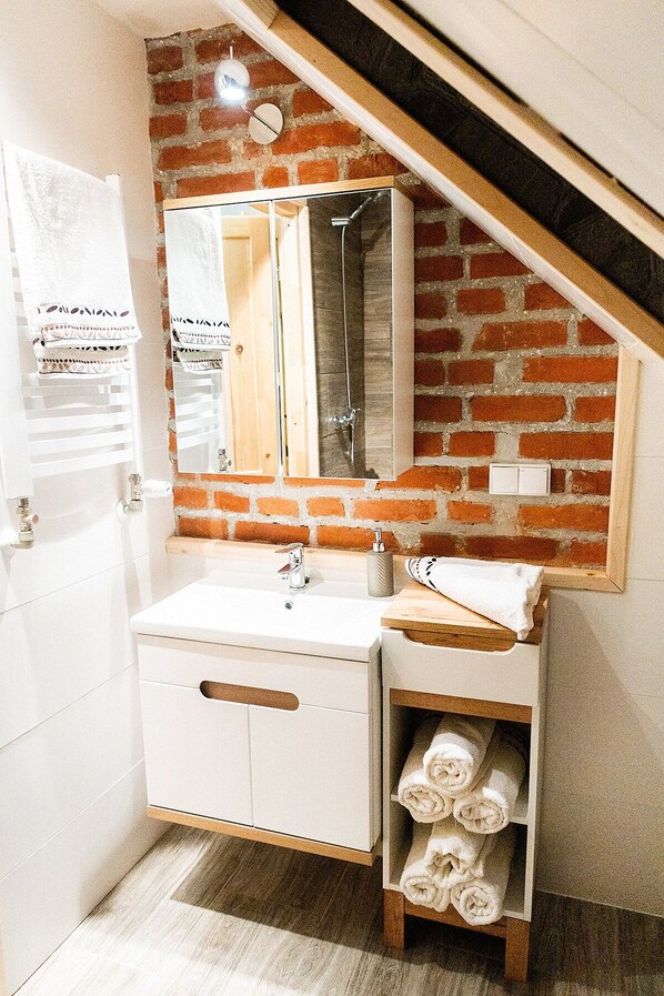 Un baño con tocador blanco, espejo, toallero y repisa con toallas.