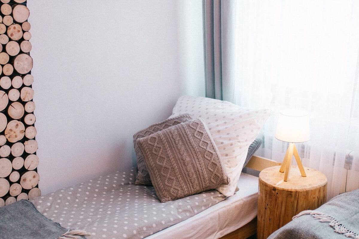 Un dormitorio pequeño y acogedor con cama, mesita de noche de madera con lámpara, alfombra de piel y televisor montado en la pared.
