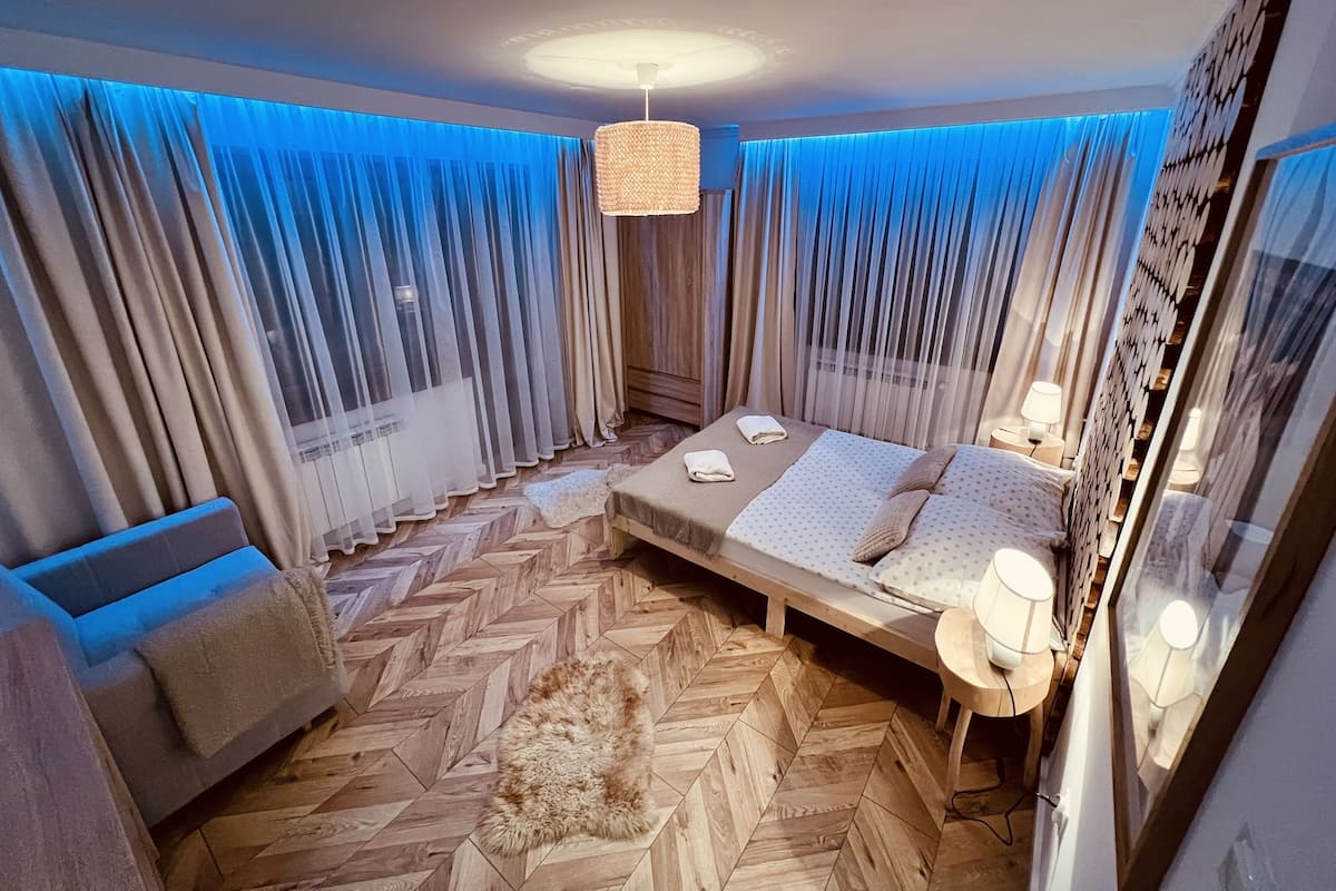 Un dormitorio moderno con una cama grande, un sofá pequeño, una alfombra y una lámpara en el techo.