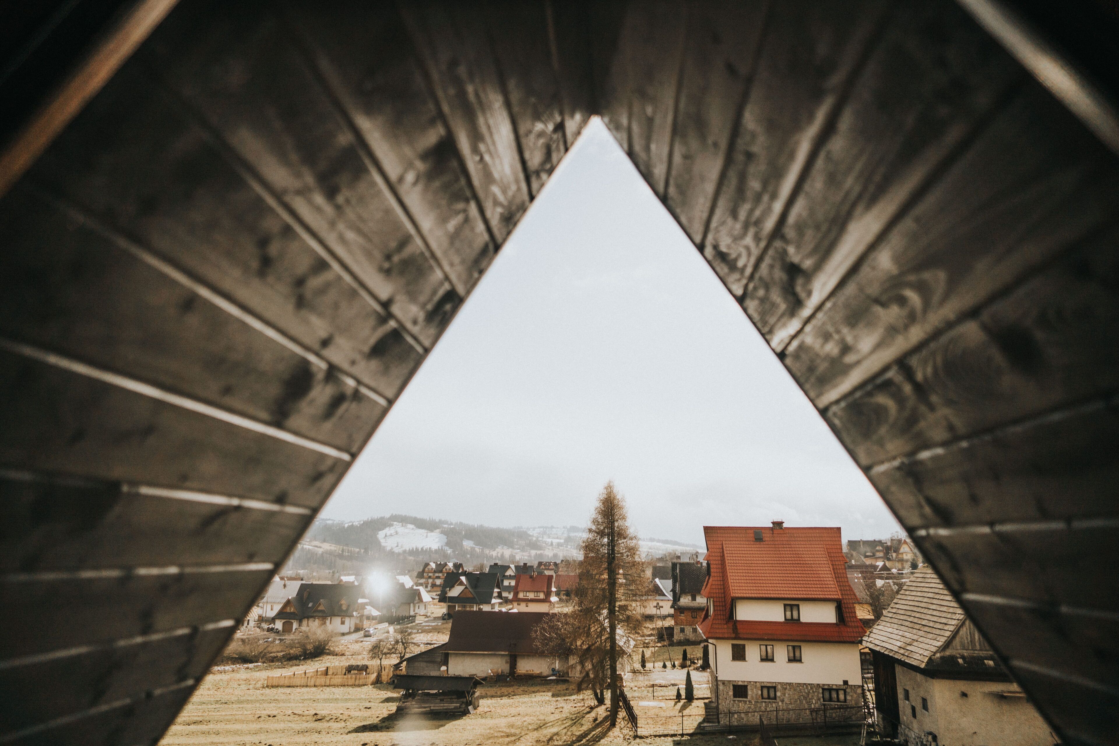 Une vue à travers une fenêtre triangulaire sur une ville avec des maisons et un paysage enneigé.