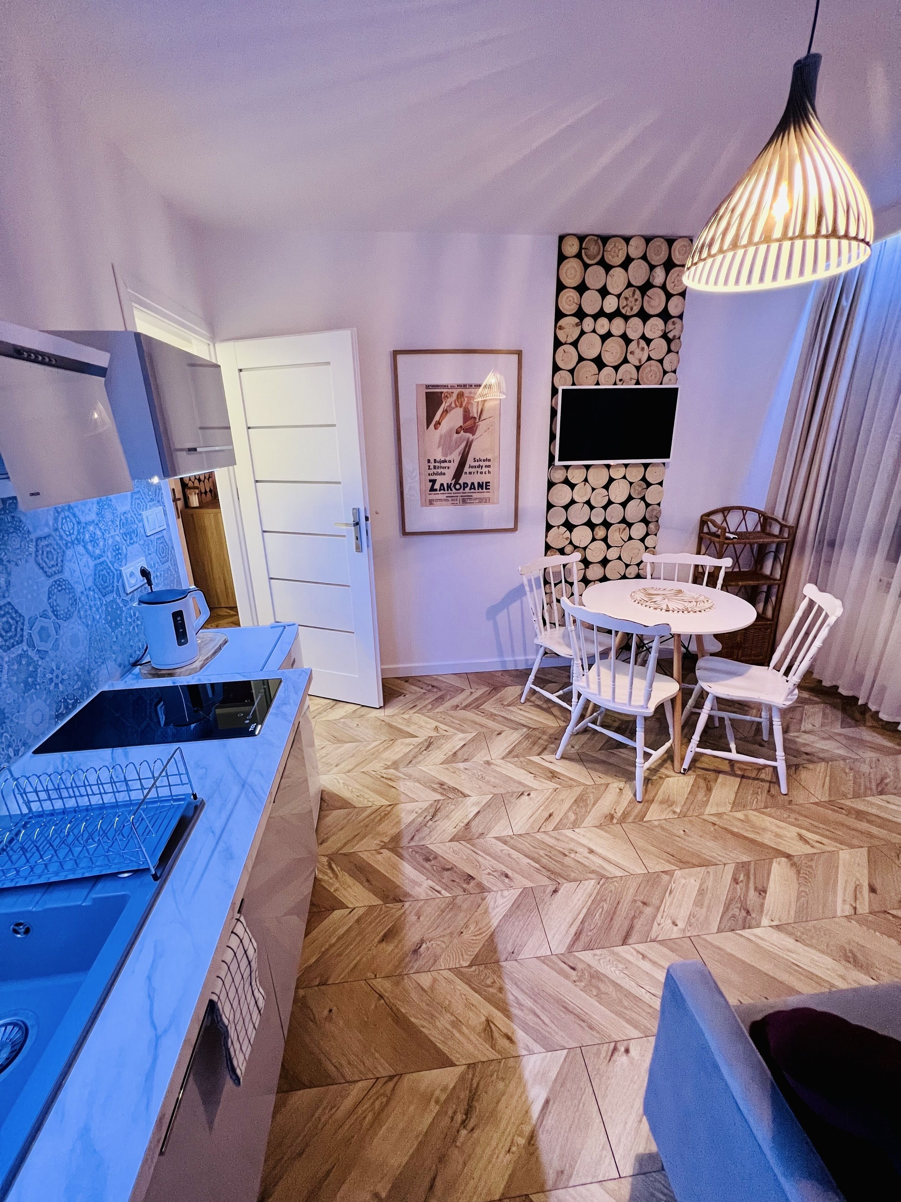 A modern kitchen with a built-in stove, a dining area with a white table and chairs, and a hanging light fixture.