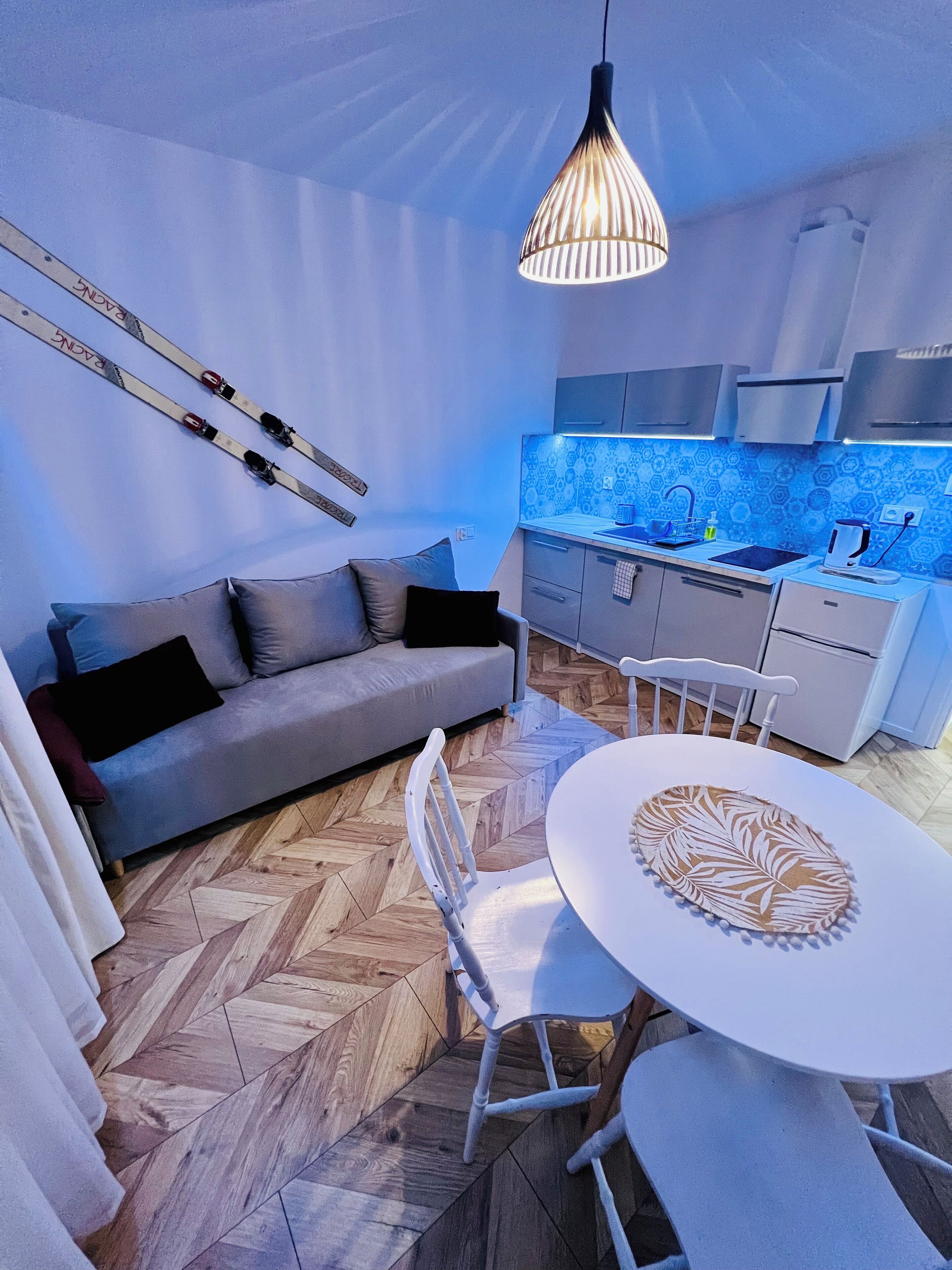 A modern living room with a sofa, a dining table, and a kitchen area with a blue backsplash.