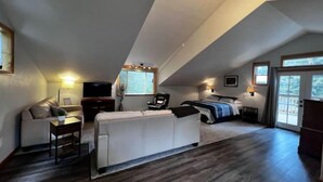 Un'ampia camera mansardata con un letto grande, un'area relax con un divano e una poltrona, e una televisione.